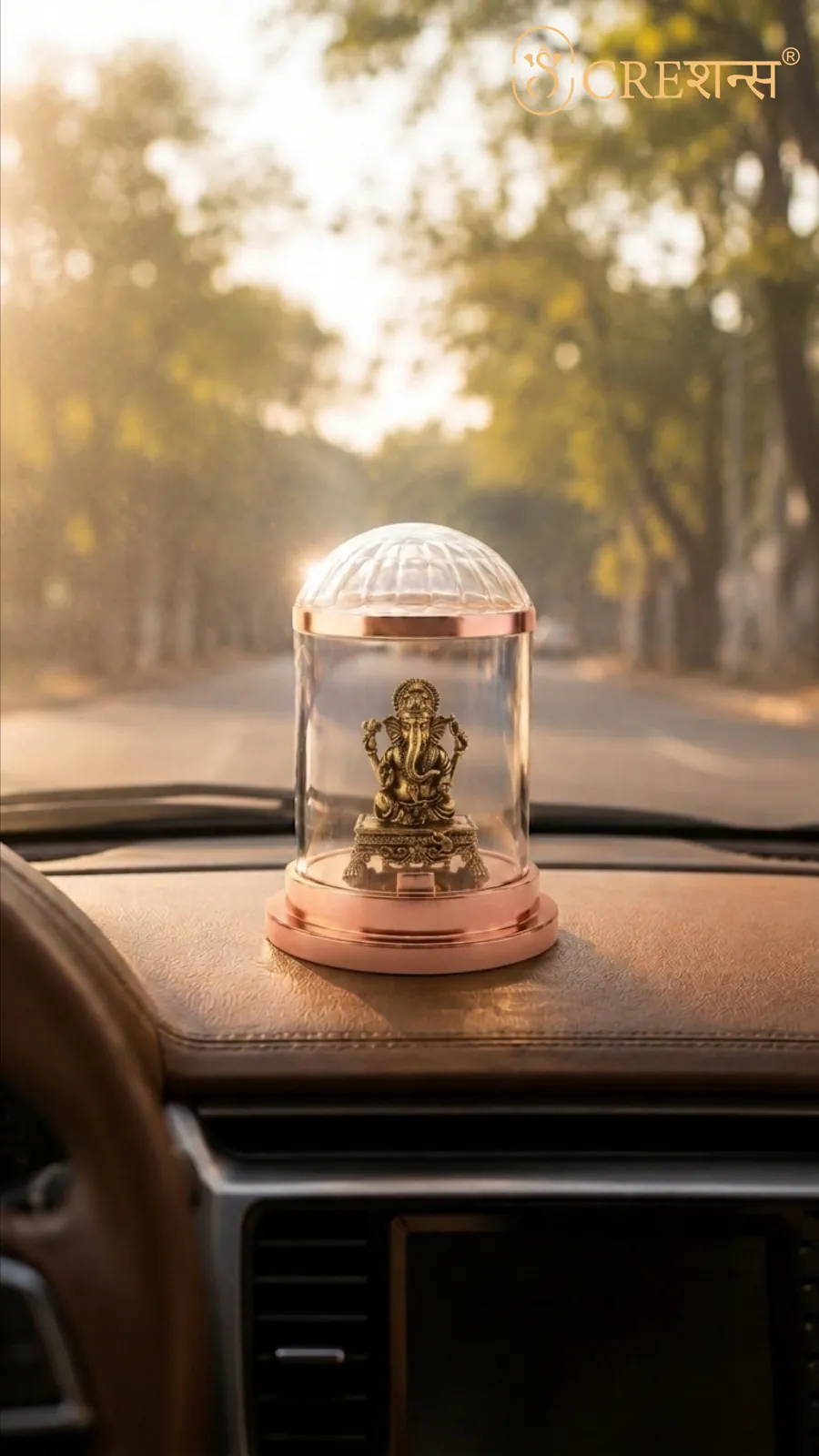 Rose-gold Ganesh cloche on a dashboard facing a tree-lined road